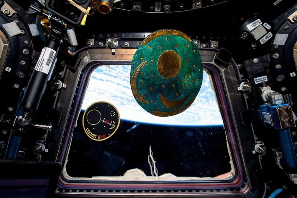 O astronauta Matthias Maurer, da Agência Espacial Europeia, colocou sua insígnia da missão 'Beijo Cósmico' e uma réplica do disco de Nebra para flutuar na cúpula de sete janelas da Estação Espacial Internacional em 2022 — Foto: MATTHIAS MAURER