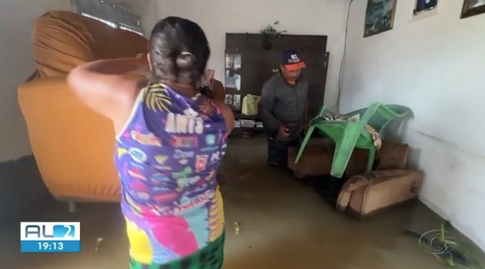 Vendedor e esposa tentam salvar sofá e outros objetos após água do rio Santo Antônio invadir a casa deles durante chuvas em São Luís do Quitunde, AL — Foto: Reprodução/TV Gazeta