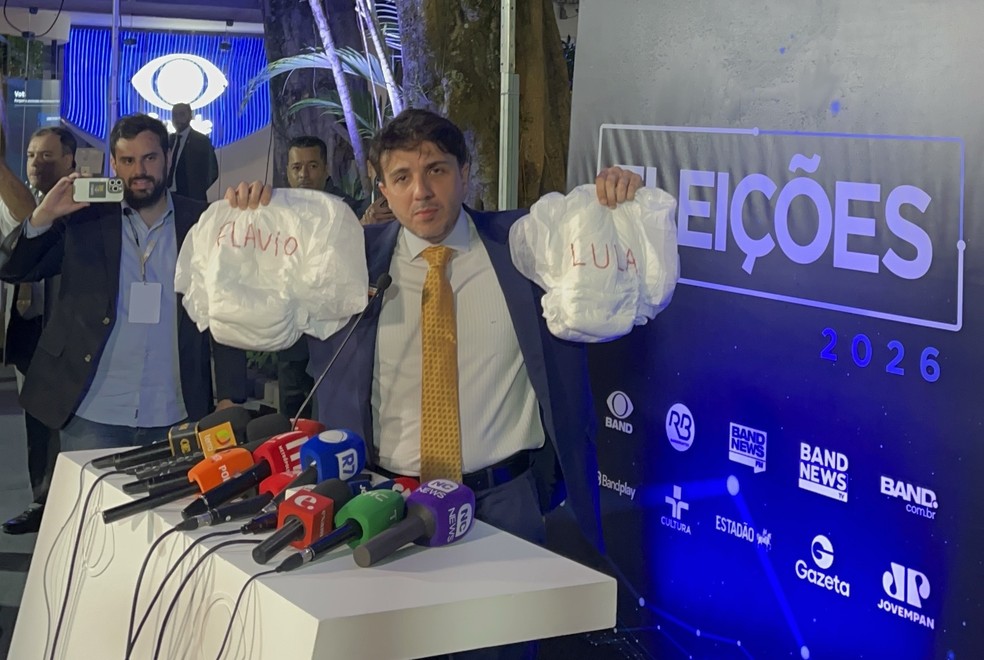 Renan Santos (Missão), segura fraldas com os nomes de Flávio e Lula ao chegar no debate da Band — Foto: Hadass Leventhal/g1