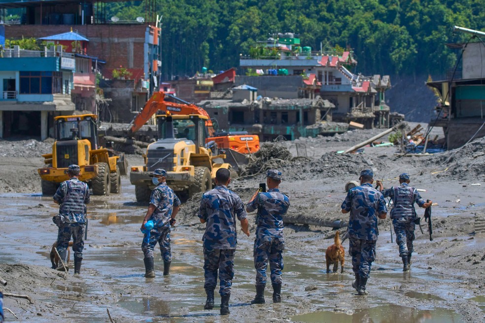 Policiais nepaleses observam máquinas removendo os destroços após enchentes repentinas no distrito de Nuwakot, Nepal, em 27 de agosto de 2026 — Foto: Niranjan Shrestha/AP