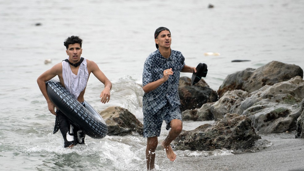 Imigrantes caminham pelas águas do Mar Mediterrâneo para tentar atravessar a fronteira entre o Marrocos e o território espanhol de Ceuta, no dia 31 de julho de 2026 — Foto: Jorge Guerrero/AFP