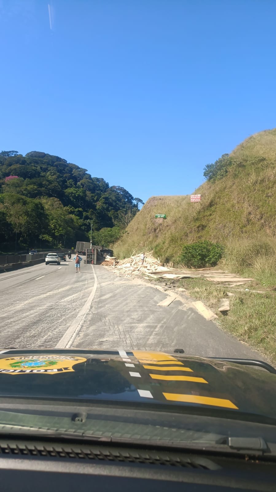 Carreta com carga de madeira tomba e deixa pessoa ferida na Via Dutra, em Piraí