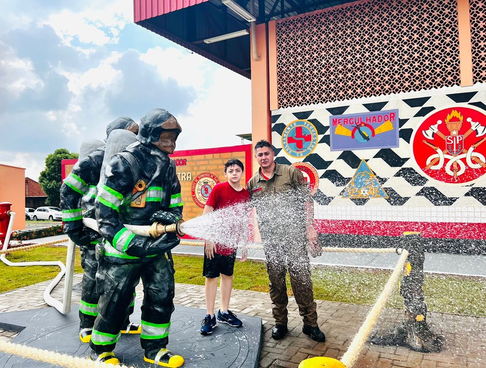 Esculturas de bombeiros enfeitam a fachada do Batalhão em Porto Ferreira (SP). Na foto, o filho Enrico e o bombeiro-artista Carlos Tomé. — Foto: Arquivo pessoal