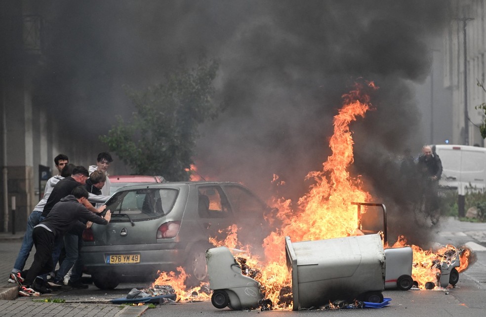 Moradores empurram um carro para longe de lixeiras em chamas durante manifestação do movimento ‘Bloquons tout’ (‘Vamos bloquear tudo’), em Nantes, no oeste da França, em 10 de setembro de 2025. — Foto: Sebastien Salom-Gomis / AFP