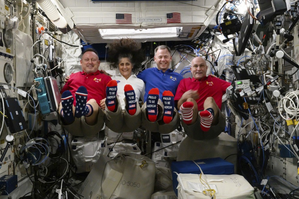 Os astronautas Butch Wilmore, Suni Williams, Nick Hague e Don Pettit mostram suas meias com tema da bandeira dos EUA a bordo da Estação Espacial Internacional no dia da eleição. Há 27 anos, o astronauta David Wolf foi o primeiro americano a votar em órbita (5/11) — Foto: Nasa via AP