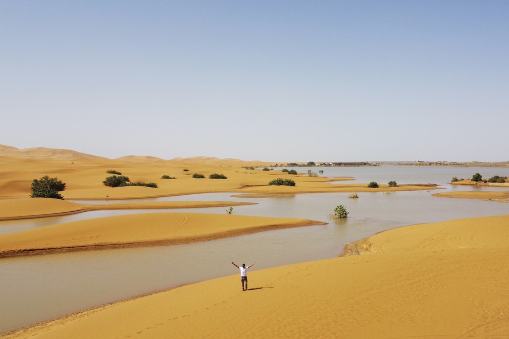 Homem caminha nas dunas de areia ao lado de lagoa formado pela intensa chuva em Merzouga, Marrocos, em 2 de outubro de 2024. — Foto: AP Photo