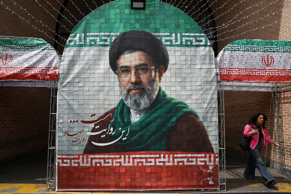 Uma mulher caminha ao lado de um banner com a foto do novo líder supremo do Irã, Mojtaba Khamenei, em Teerã — Foto: Majid Asgaripour/WANA via Reuters