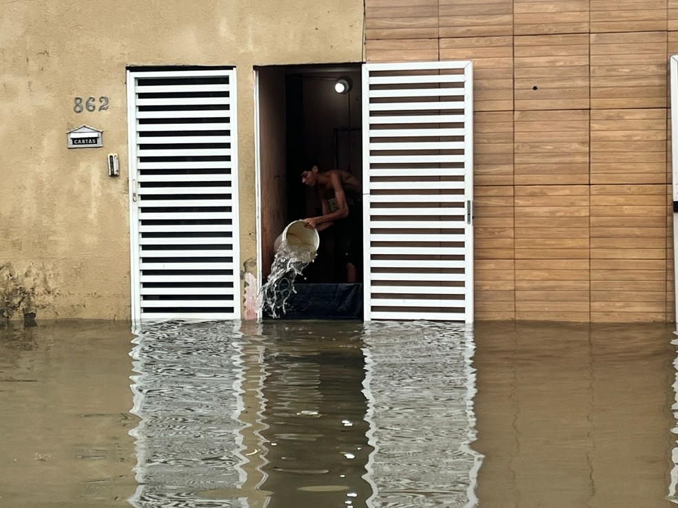 Morador tenta tirar água de dentro de casa usando um balde na Rua Santa Clara, em Felipe Camarão — Foto: Vinicius Marinho/Inter TV Cabugi