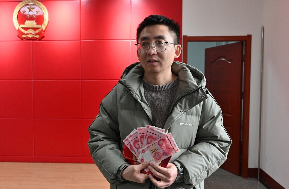 Chinês com o dinheiro recebido após casar — Foto: Adek BERRY / AFP