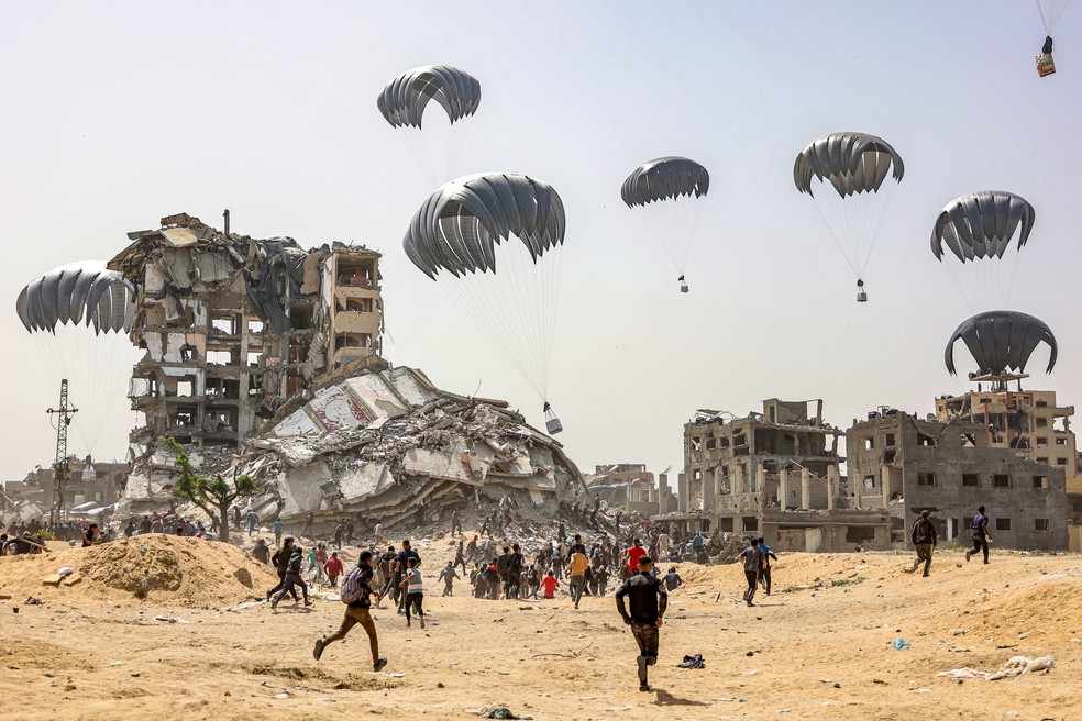 23 de abril - Pessoas correm para apanhar pacotes de ajuda humanitária lançados sobre o norte da Faixa de Gaza em meio ao conflito em andamento no território palestino entre Israel e o grupo militante Hamas — Foto: Omar Al-Qattaa/AFP