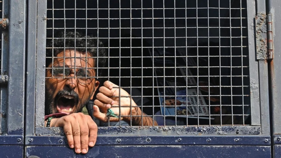 Um manifestante grita palavras de ordem de dentro de uma viatura policial após ser detido durante protesto em Mumbai — Foto: Getty Images via BBC