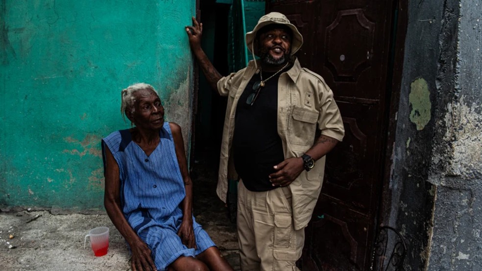 O líder de gangue Jimmy Chérizier, conhecido como Barbecue, ao lado de uma moradora de uma região de Porto Príncipe controlada por ele, no dia 6 de julho de 2026 — Foto: Clarens Siffroy