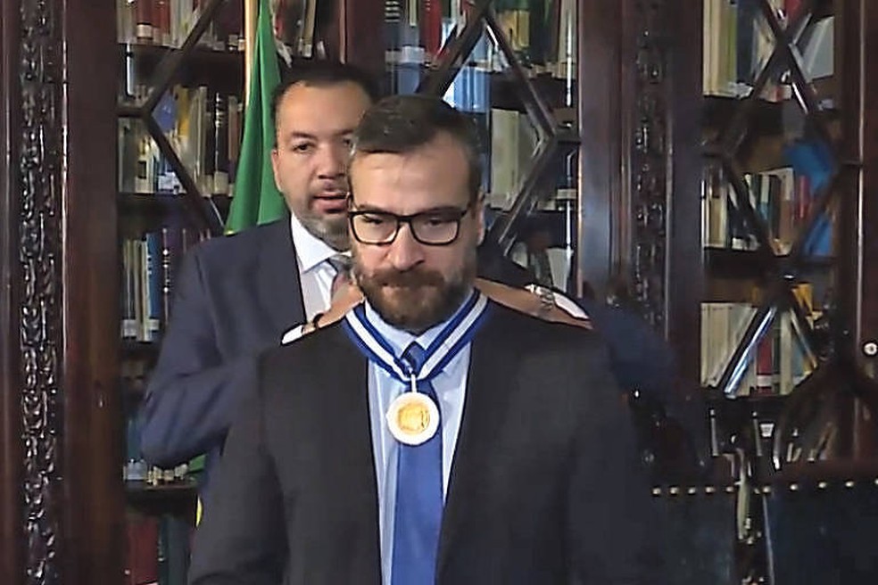 À esquerda, o ex-deputado Márcio Canella (União) coloca a Medalha Tiradentes no delegado Marcus Amim, ex-secretário de Polícia Civil do RJ, em 2018 — Foto: Reprodução/TV Alerj