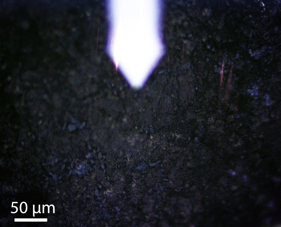 Imagem mostra fragmento do asteroide Bennu analisado em microscópio, revelando em detalhe regiões onde água, minerais e moléculas orgânicas coexistiram. — Foto: Mehmet Yesiltas