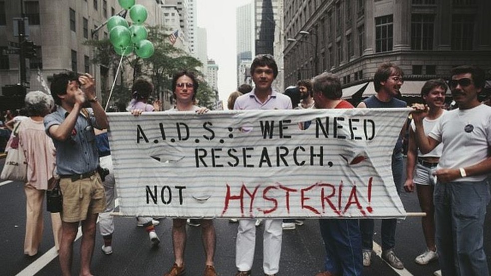 Em 1983, homens erguem um cartaz com os dizeres: 'Aids: nós precisamos de pesquisa, não de histeria' — Foto: Getty Images via BBC