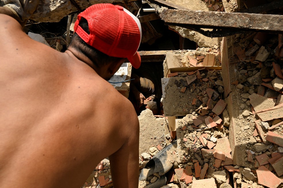 Pessoas trabalham para resgatar um homem preso sob os escombros de um prédio que desabou, após os terremotos em La Guaira, Venezuela, em 25 de junho de 2026 — Foto: REUTERS/Maxwell Briceno