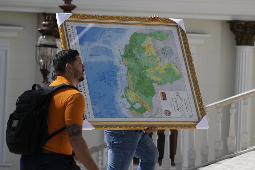 Morador carrega quadro com novo mapa divulgado na Venezuela contendo a região de Essequibo — Foto: Ariana Cubillos/AP