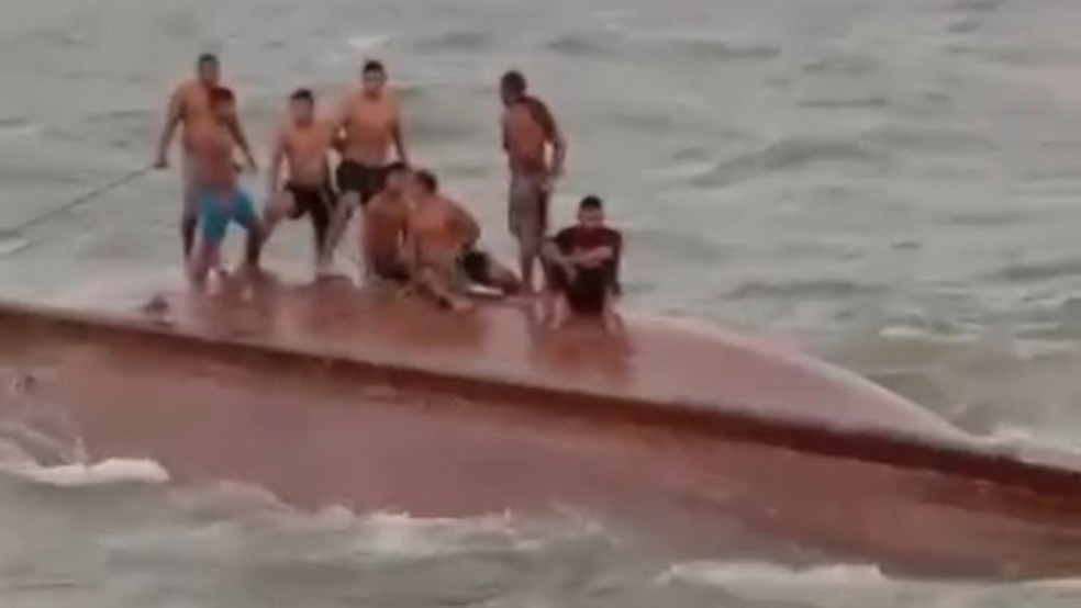 Pescadores ficaram em pé e sentados no casco do barco enquanto tripulantes de outra embarcação tentavam resgatá-los. — Foto: Reprodução / Redes sociais