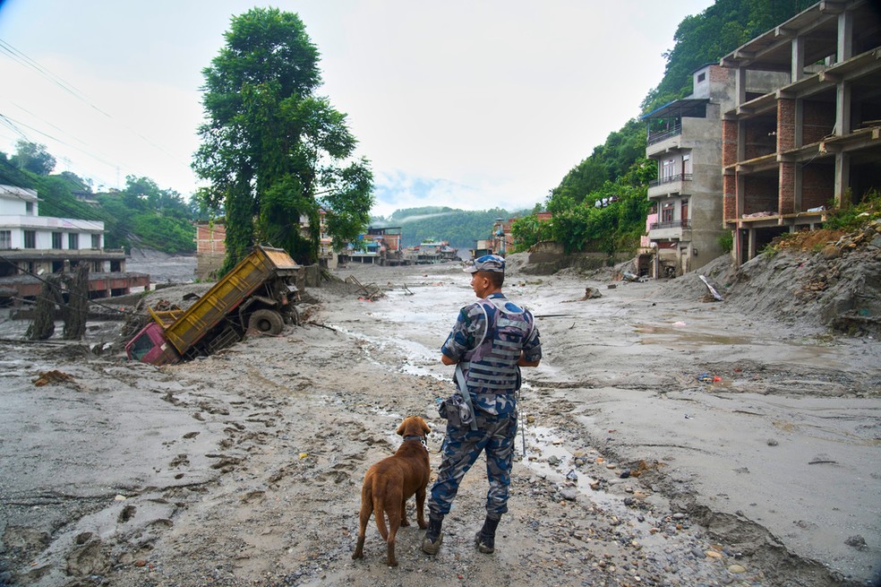 Um policial com um cão farejador observa os danos deixados pelas enchentes repentinas em Devighat, no distrito de Nuwakot, no Nepal, na quinta-feira, 27 de agosto de 2026 — Foto: AP Photo/Niranjan Shrestha