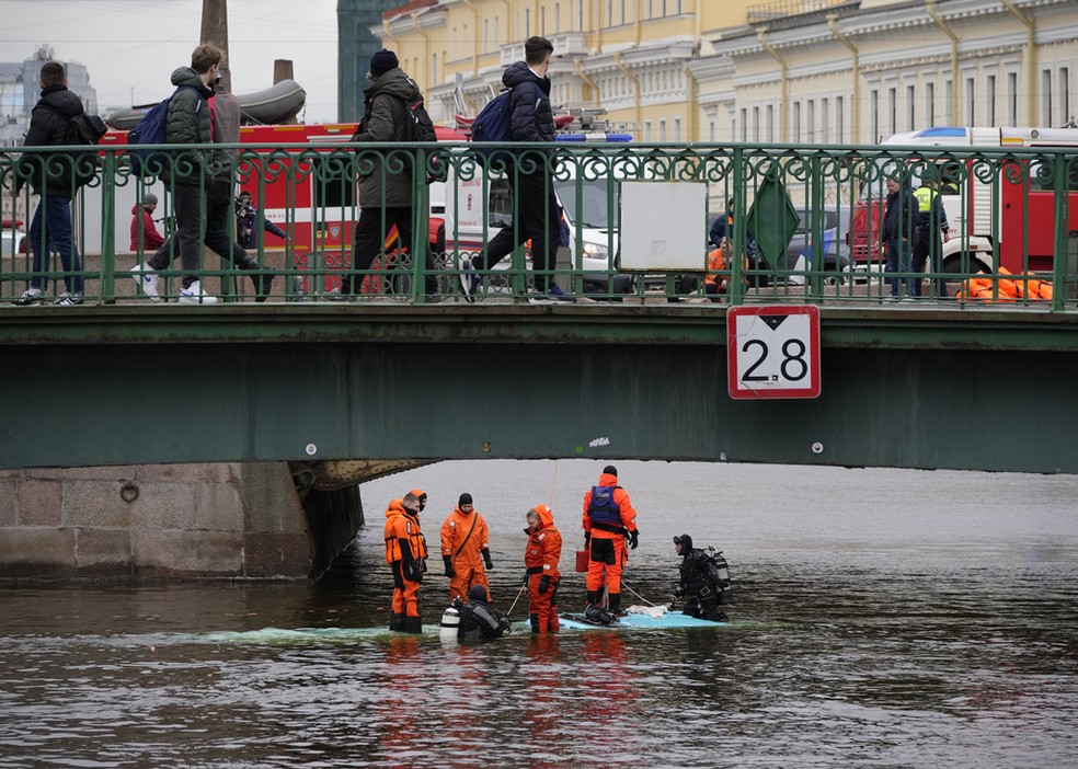 Equipes de resgate ficam de pé em cima de ônibus que caiu de ponte em São Petersburgo, na Rússia, em 10 de maio de 2024. — Foto: Dmitri Lovetsky/ AP