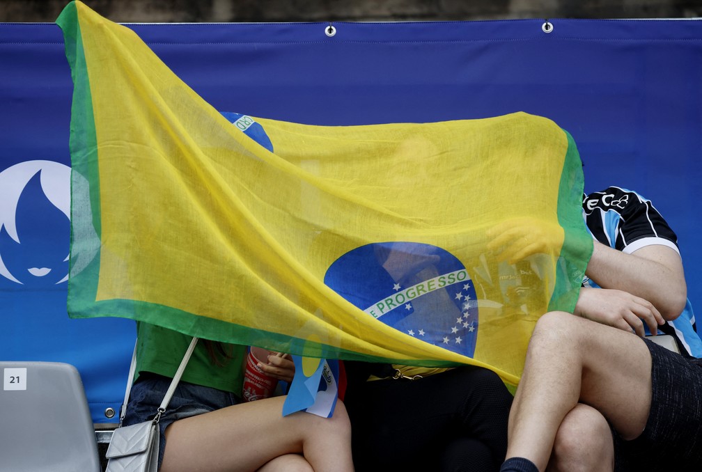 Torcedores brasileiros se protegem da chuva enquanto aguardam a cerimônia de abertura das Olimpíadas 2024 — Foto: Adnan Abidi/Reuters