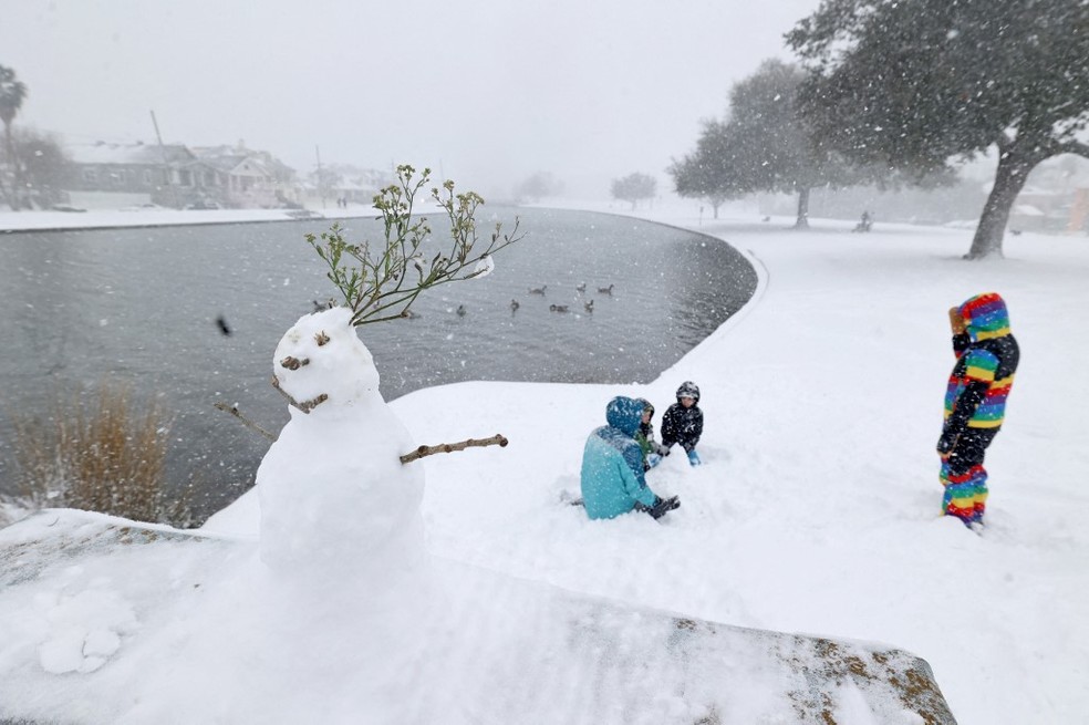 Crianças brincam perto de boneco de neve feito em Nova Orleans, Louisiana, nos EUA — Foto: Michael DeMocker/Getty Images via AFP