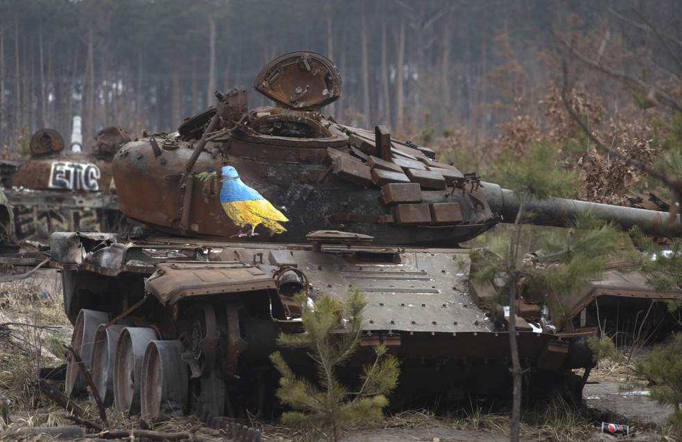 Obra do artista italiano Tvboy sobre a carcaça de um tanque de guerra destruído na vila de Dmytrivka, perto de Kiev, mostra um pombo com as cores da bandeira ucraniana e um ramo no bico — Foto: Efrem Lukatsky/AP