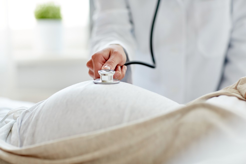 Médico ausculta barriga de mulher grávida — Foto: Adobe Stock