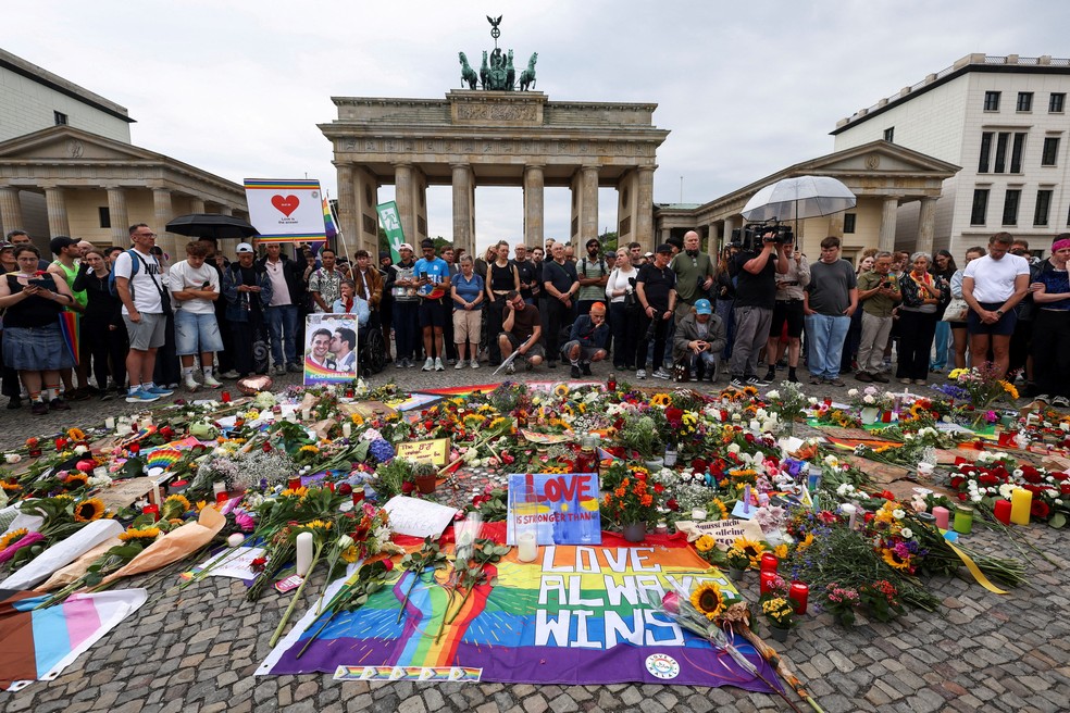 Pessoas se reúnem ao redor de flores, lembranças e velas deixadas por outras pessoas no Portão de Brandemburgo, após um incidente fatal em que um veículo colidiu com a multidão próximo à parada anual do Christopher Street Day Pride em Berlim na noite de sábado, deixando várias pessoas feridas e fazendo com que a parada fosse cancelada, em Berlim, Alemanha, 26 de julho de 2026. REUTERS/Christian Mang TPX IMAGENS DO DIA — Foto: Reuters