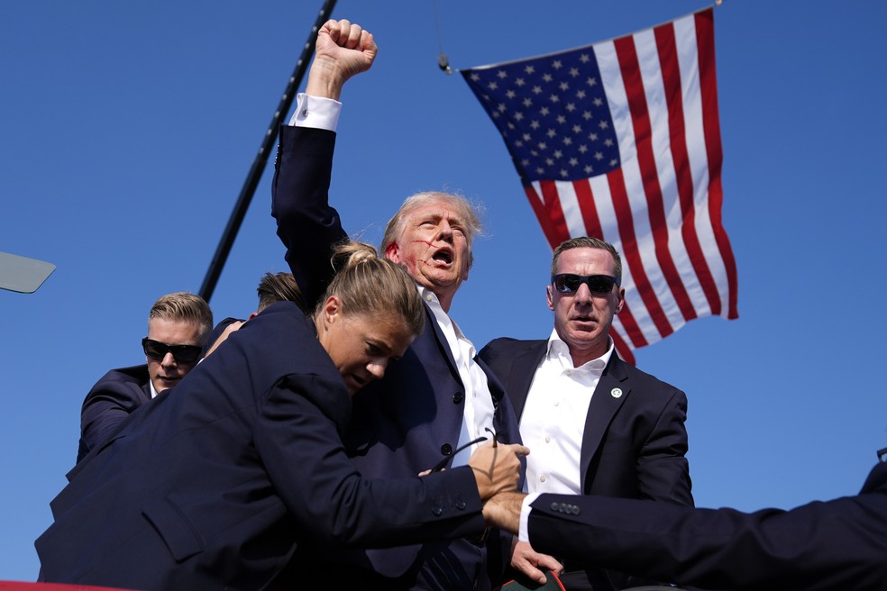 Donald Trump ergue o punho enquanto é cercado por agentes do Serviço Secreto dos EUA após ser alvejado por um tiro na orelha em um comício eleitoral em 13 de julho de 2024. — Foto: AP Foto/Evan Vucci