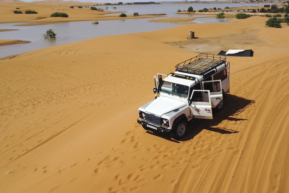Veículo transporta turistas nas dunas de areia ao lado de lagoa formada pela intensa chuva em Merzouga, Marrocos, em 2 de outubro de 2024. — Foto: AP Photo