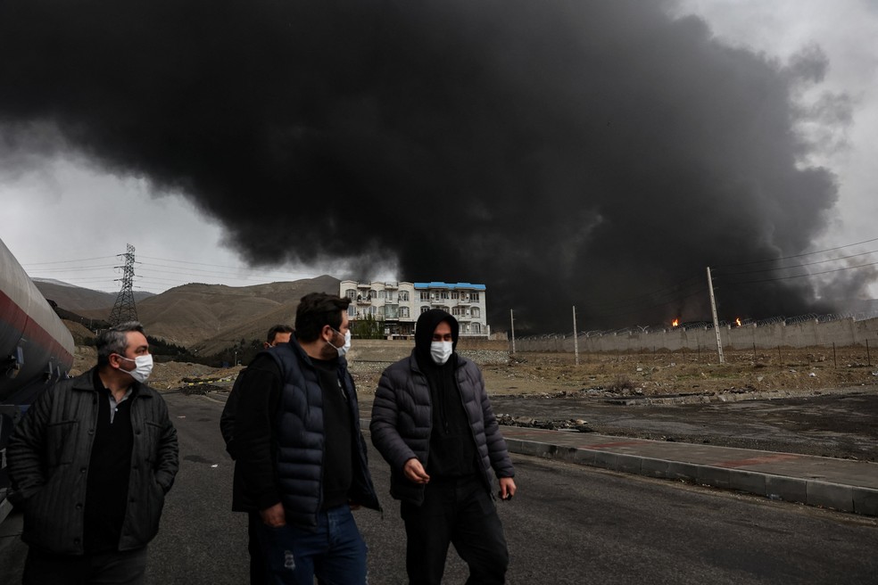 Pessoas caminham enquanto fumaça sobe ao fundo após ataque a tanques de combustível em Shahran, em meio ao conflito entre EUA e Israel com o Irã, em Teerã — Foto: Reuters