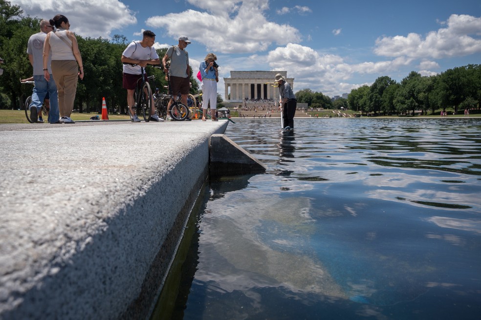 Visitantes observam enquanto um funcionário do Serviço Nacional de Parques usa um aspirador para limpar o espelho d'água do Lincoln Memorial, em Washington, na sexta-feira (19) — Foto: Mark Schiefelbein/AP Photo