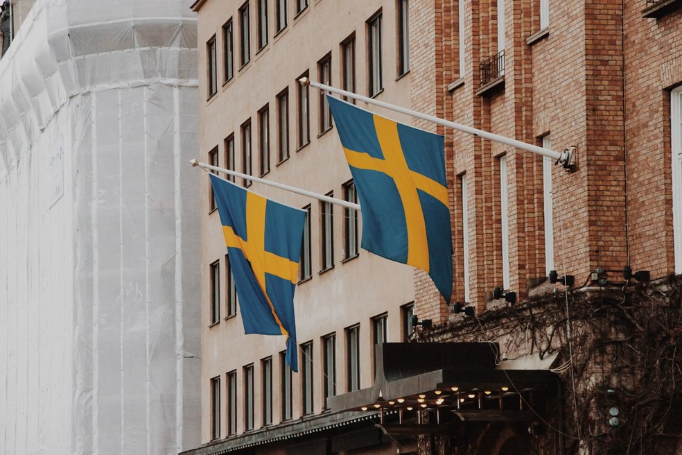 Bandeiras da Suécia penduradas em fachada de prédio em Estocolmo — Foto: Unsplash/Cartist