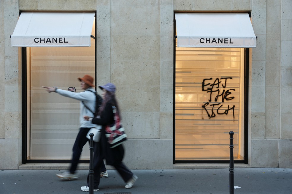 Pessoas caminham em frente a loja de luxo com escrito "Coma os ricos" em Paris, após os protestos de sábado (17). — Foto: Stephanie Lecocq/Reuters