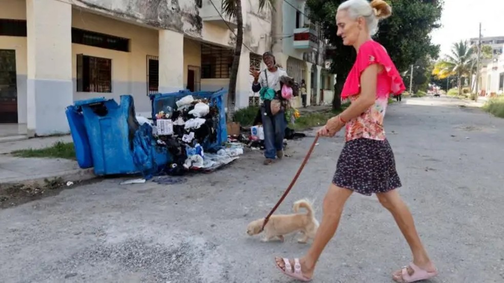 Em Havana, pessoas caminham ao lado de uma grande lixeira incendiada na noite anterior em protesto contra os prolongados apagões. — Foto: EPA/Shutterstock via BBC