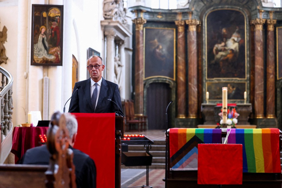 O chanceler alemão Friedrich Merz fala ao lado de um altar coberto com bandeiras do arco-íris durante um serviço memorial na Igreja de St. Mary após um incidente fatal em que um veículo atropelou uma multidão perto do desfile anual da Parada do Orgulho Christopher Street Day em Berlim na noite de sábado, deixando várias pessoas feridas e fazendo com que o desfile fosse cancelado, em Berlim, Alemanha, 26 de julho de 2026. REUTERS/Christian Mang TPX IMAGENS DO DIA — Foto: Reuters