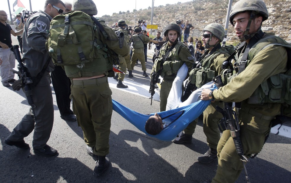 Soldados israelenses carregam um palestino ferido em briga durante um protesto na estrada 443, perto da aldeia de Beit Ur, na Cisjordânia. Palestinos bloquearam a estrada para protestar contra ataques dos colonos judeus dos palestinos em suas propriedades — Foto: Nasser Shiyoukhi/AP