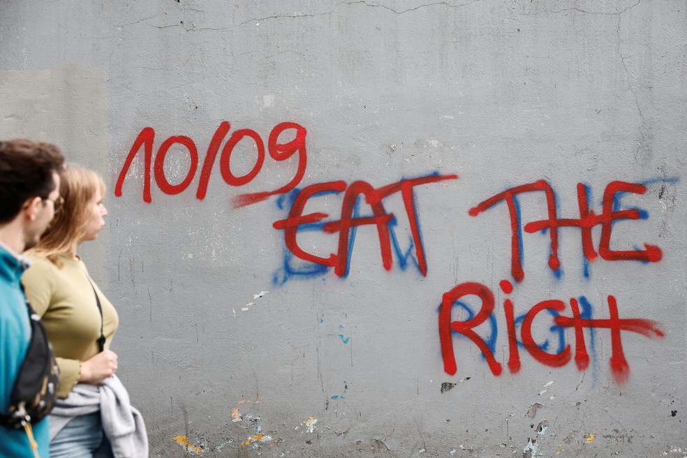 Pessoas passam por um muro com o slogan '10/09 comam os ricos' pintado, em uma rua durante um dia de protestos em Paris, como parte de um movimento de protesto popular chamado 'Bloquons Tout' ('Vamos Bloquear Tudo'), que pede interrupções nacionais durante todo o dia. — Foto: Benoit Tessier/Reuters