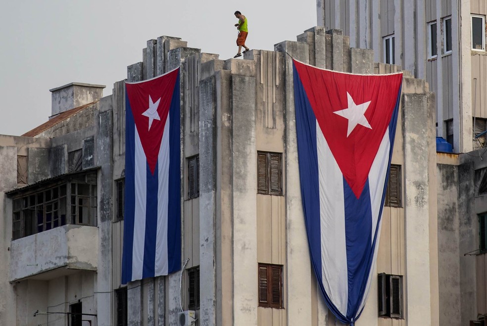Un hombre es visto después de extender dos banderas cubanas gigantes a los lados de un edificio vecino a la Embajada de Estados Unidos — Foto: Ramón Espinosa/AP