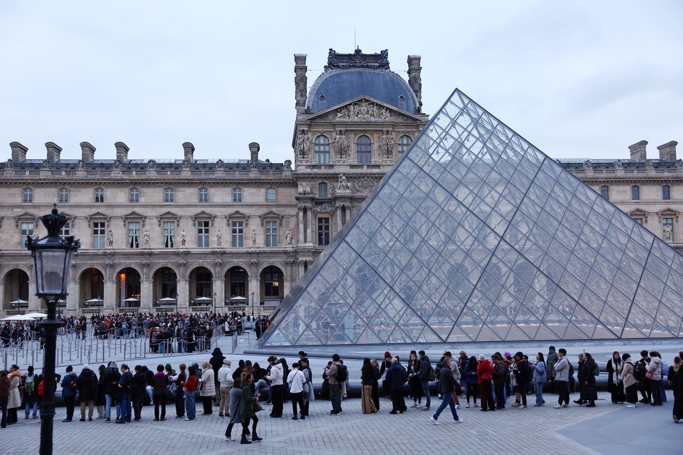 Pessoas fazem fila perto da Pirâmide de Vidro do Museu do Louvre para entrar no museu, que permanece fechado enquanto seus funcionários continuam as discussões sobre a possibilidade de estender uma greve por melhores salários e condições de trabalho neste 17 de dezembro de 2025 — Foto: Reuters/Abdul Saboor