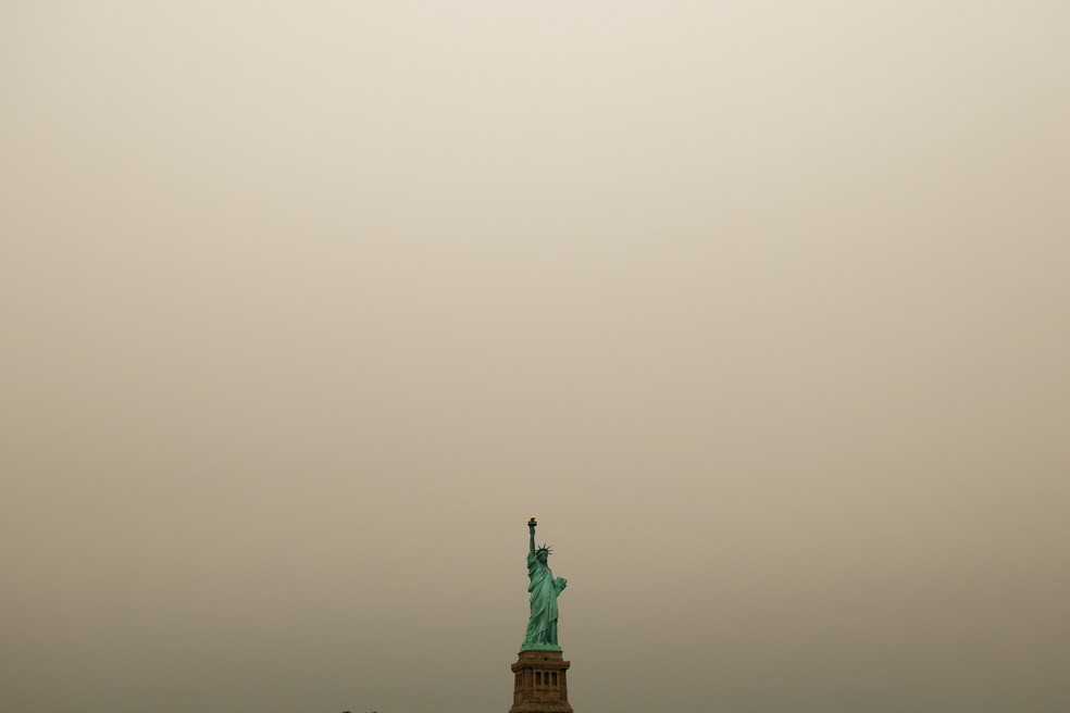 A Estátua da Liberdade no porto de Nova York é vista através de uma camada de fumaça de incêndio florestal em Jersey City, Nova Jersey, EUA, em 16 de julho de 2026. — Foto: REUTERS/Mike Segar