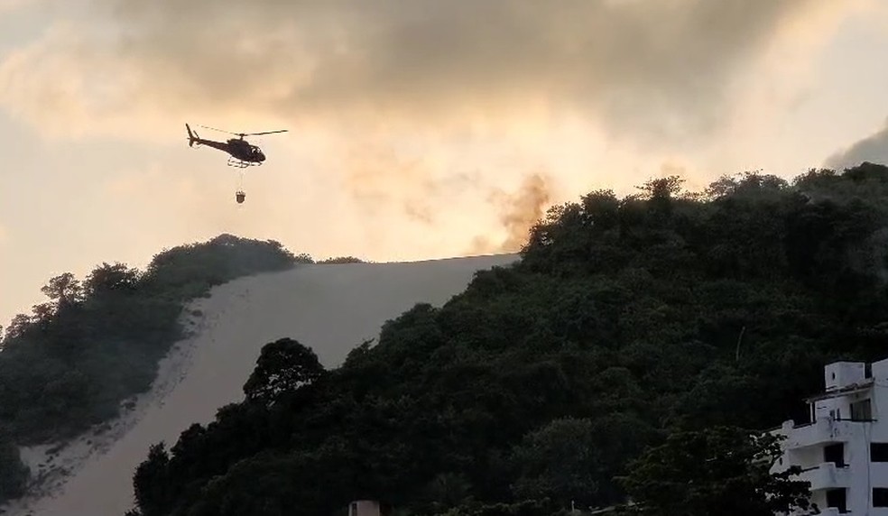 Helicóptero Potiguar I busca água do mar para jogar sobre os focos de incêndio no Morro do Careca — Foto: Reprodução