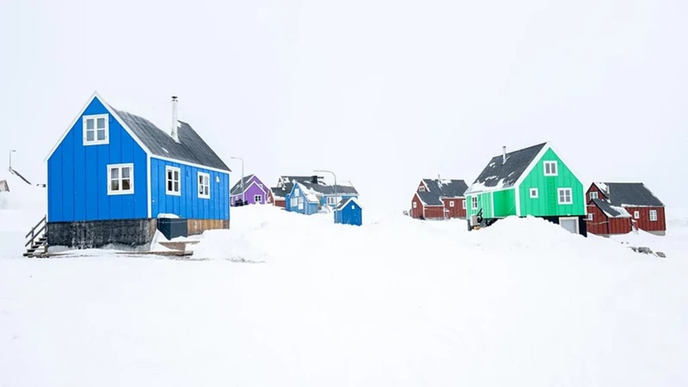 Casas pintadas com cores vivas, em pé na neve branca profunda, dominam a paisagem — Foto: Kevin Hall