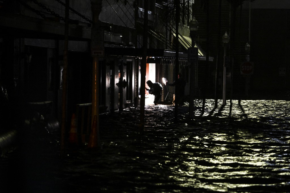 Moradores usam celulares para tirar fotos e iluminar o caminho enquanto caminham por ruas alagadas pelo furacão Milton em Fort Myers, na Flórida — Foto: Chandan Khanna/AFP