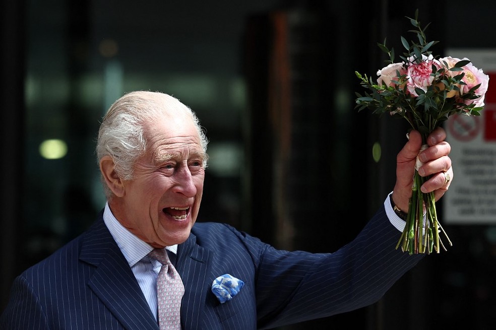 Rei Charles III segura um ramo de flores e acena durante visita a centro de tratamento de câncer em Londres — Foto: HENRY NICHOLLS / AFP