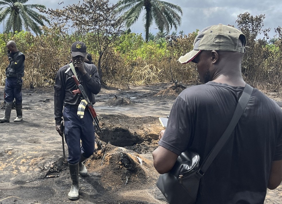 Pessoas caminham ao lado de corpos carbonizados do lado de fora de refinaria que explodiu em Emohua, na Nigéria, em 3 de outubro de 2023 — Foto: Associated Press