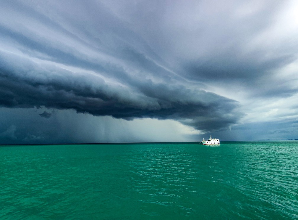 A fotografia 'Nature and Boat', tirada no Mar de Andaman, na costa de Mianmar, mostra a aproximação de uma tempestade. Um barco de pesca solitário na imagem navega na ainda calma água turquesa da região. — Foto: Htet Phyo Wai