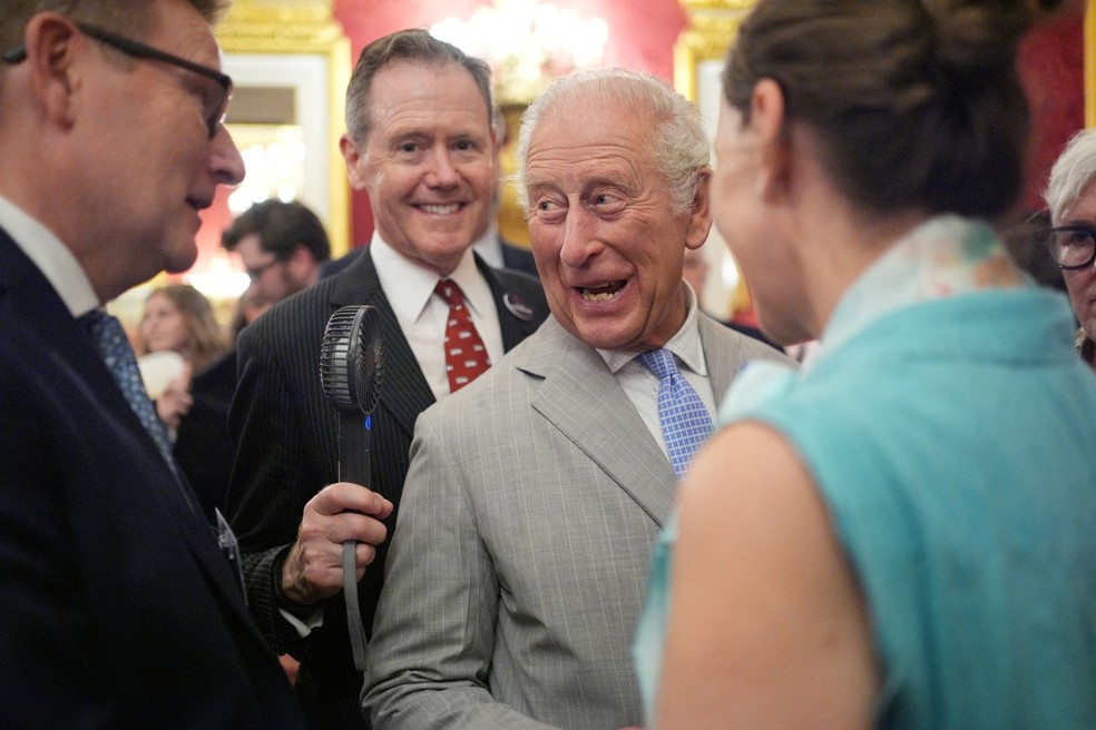 O vice-almirante Sir Tony Johnstone-Burt, mestre da casa do Soberano, segura um pequeno ventilador a bateria para o rei Carlos III da Grã-Bretanha durante uma recepção da Semana do Clima de Londres — Foto: CHRIS JACKSON / POOL / AFP