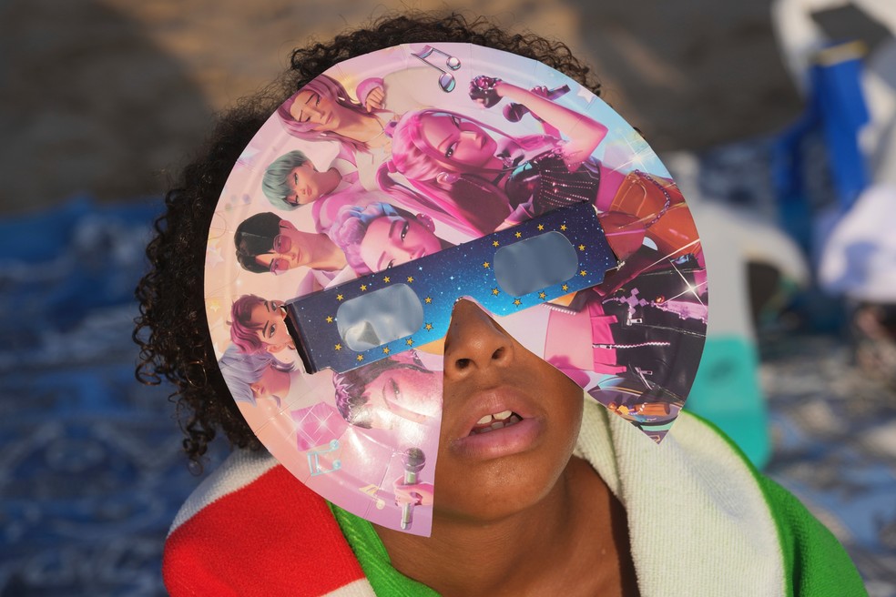 Banhista usa óculos especiais para observar o início do eclipse solar na praia de Puerto de Sagunto, perto de Valência, na Espanha, nesta quarta-feira (12). — Foto: Alberto Saiz/AP